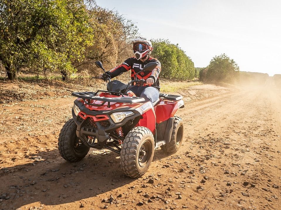 A man quad biking featuring full biking gear, dusty road, and surrounded by tall green trees.