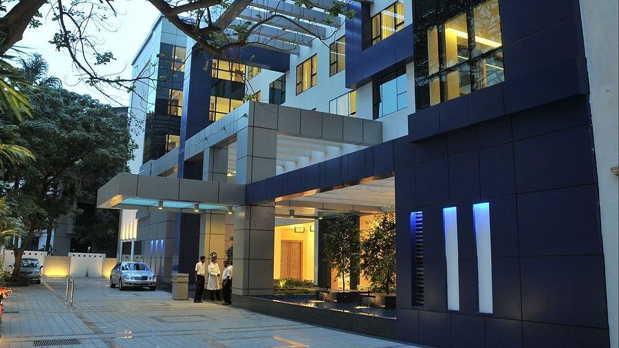 The exterior of a modern, multi-story building with blue and grey accents, illuminated at dusk - Adarsh Hamilton.