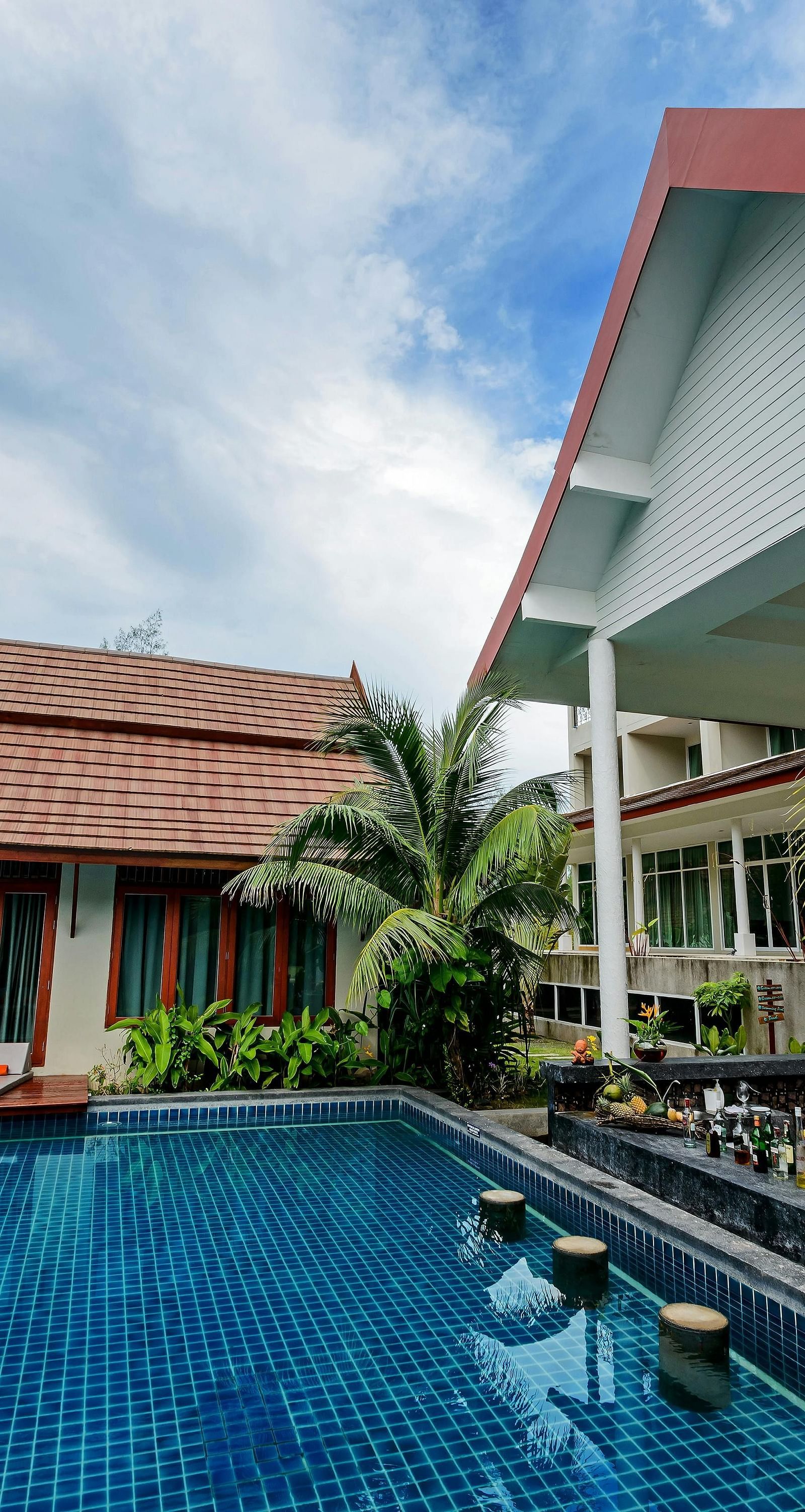 facade image of a resort overlooking a clear blue swimming pool surrounded by green plants in the corner