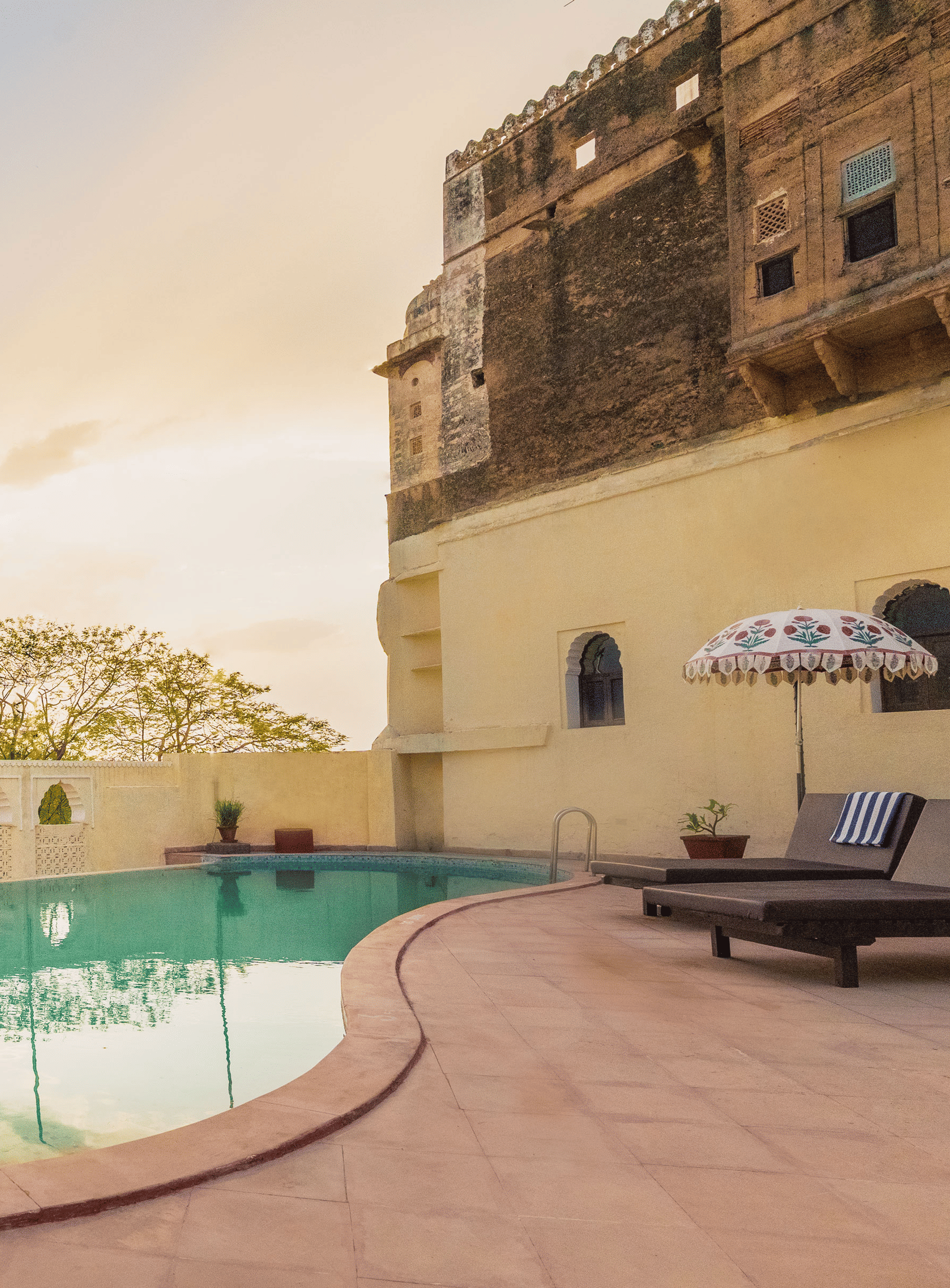 A tranquil pool at Fort Barli, flanked by historic walls and lounge chairs, offers a serene escape with a touch of grandeur.