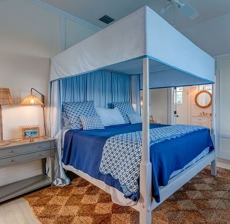 Bedroom with a blue canopy bed, wooden nightstand, and soft lighting | Abaco Inn