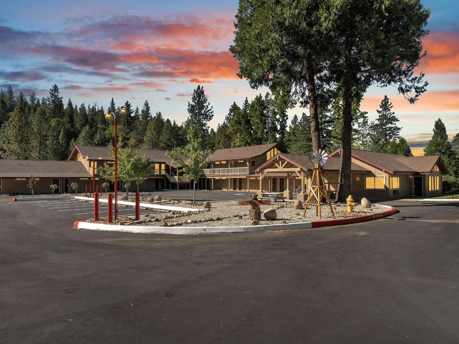 A wide view of the exterior of a hotel with green foliage in the background along with hued sky.