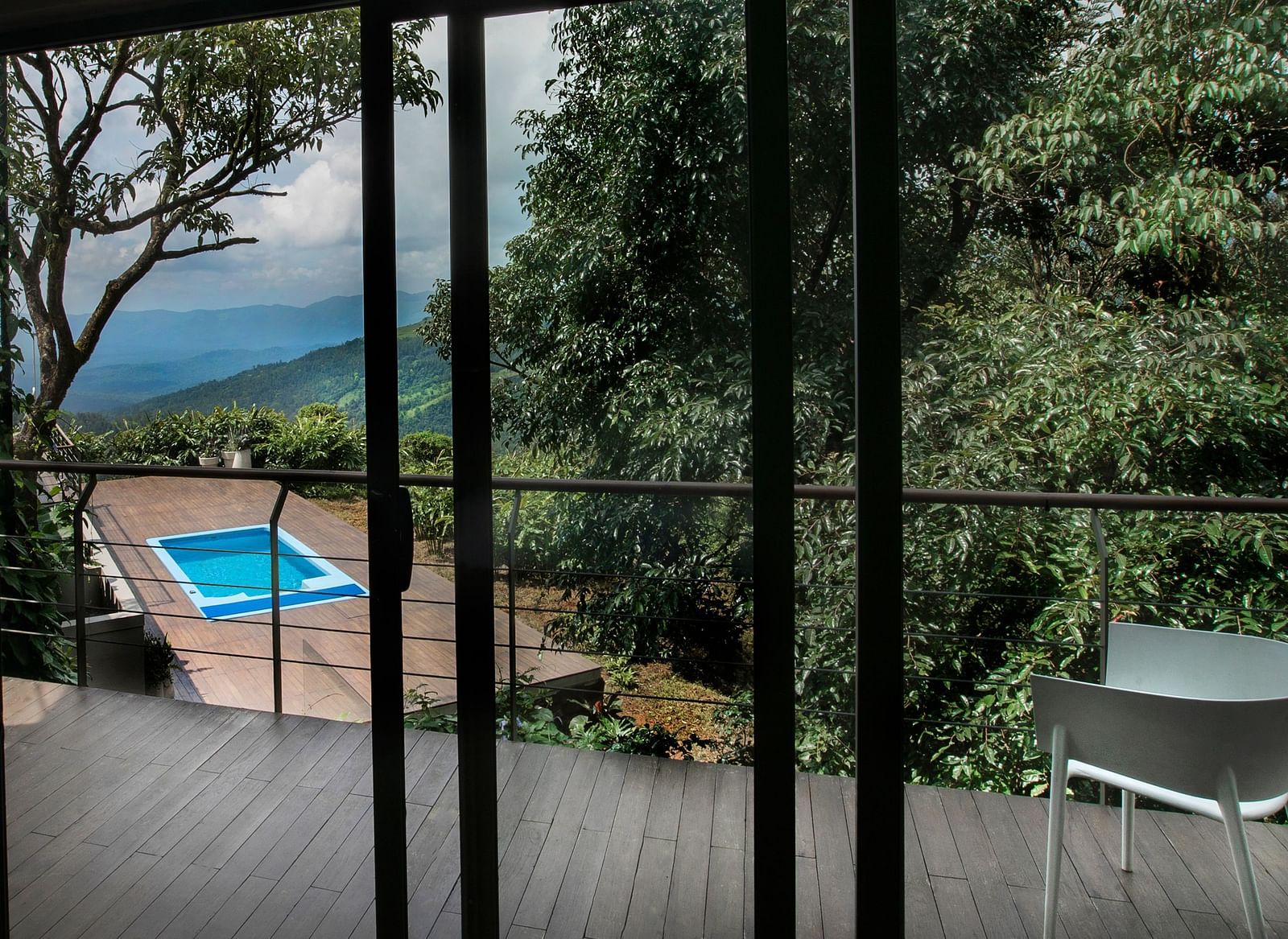 A balcony featuring a chair, with a serene view of lush trees ahead and a swimming pool below, at Stanley Revelation.