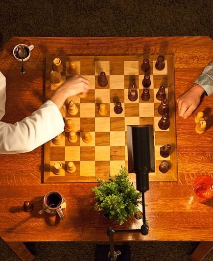 Overhead view of two people playing chess on a wooden table with warm lighting - Brewery Gulch Inn & Spa