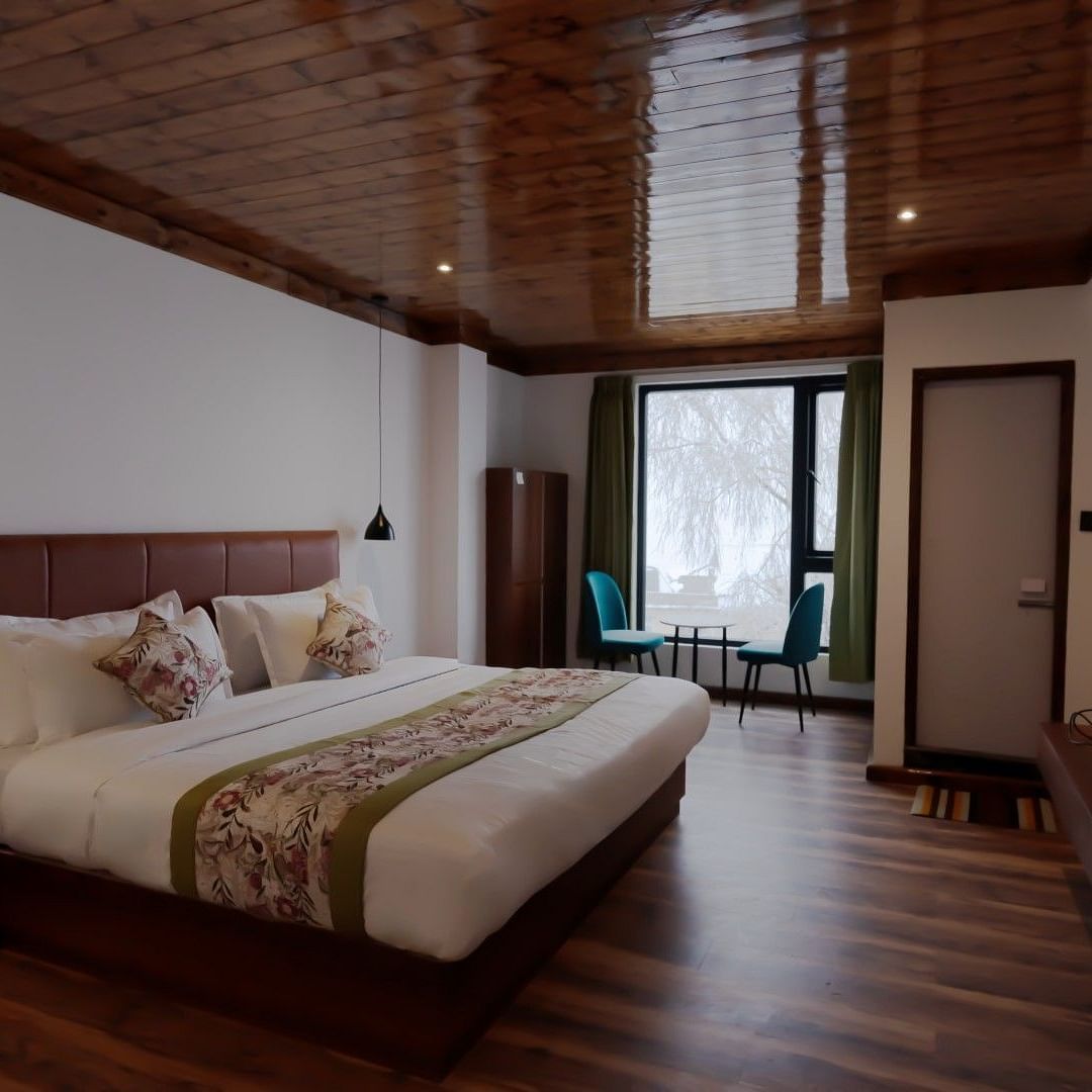 An image of a bedroom with wooden floor and ceiling, flat TV screen, a seating area and a balcony - Avianna Group of Hotels & Resorts