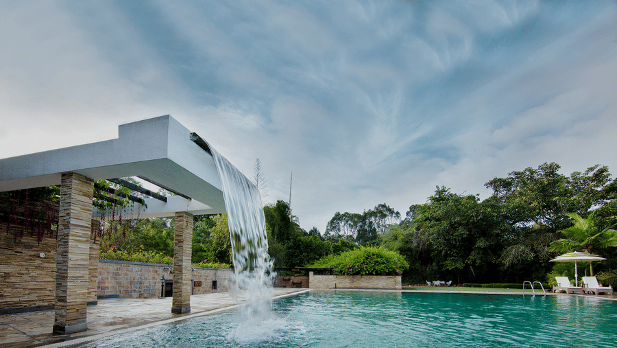 A modern pool with blue water and cloudy skies at Amanvana Spa Resort, Coorg - Luxury Resort