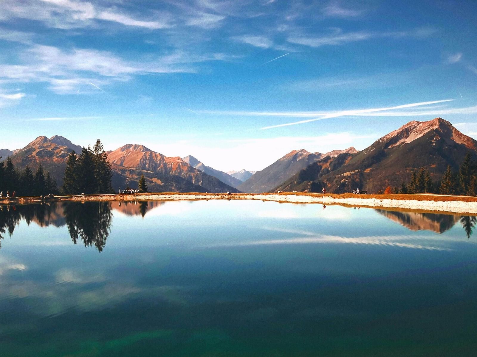 A serene mountain landscape featuring a reflective lake surrounded by towering peaks and lush trees.