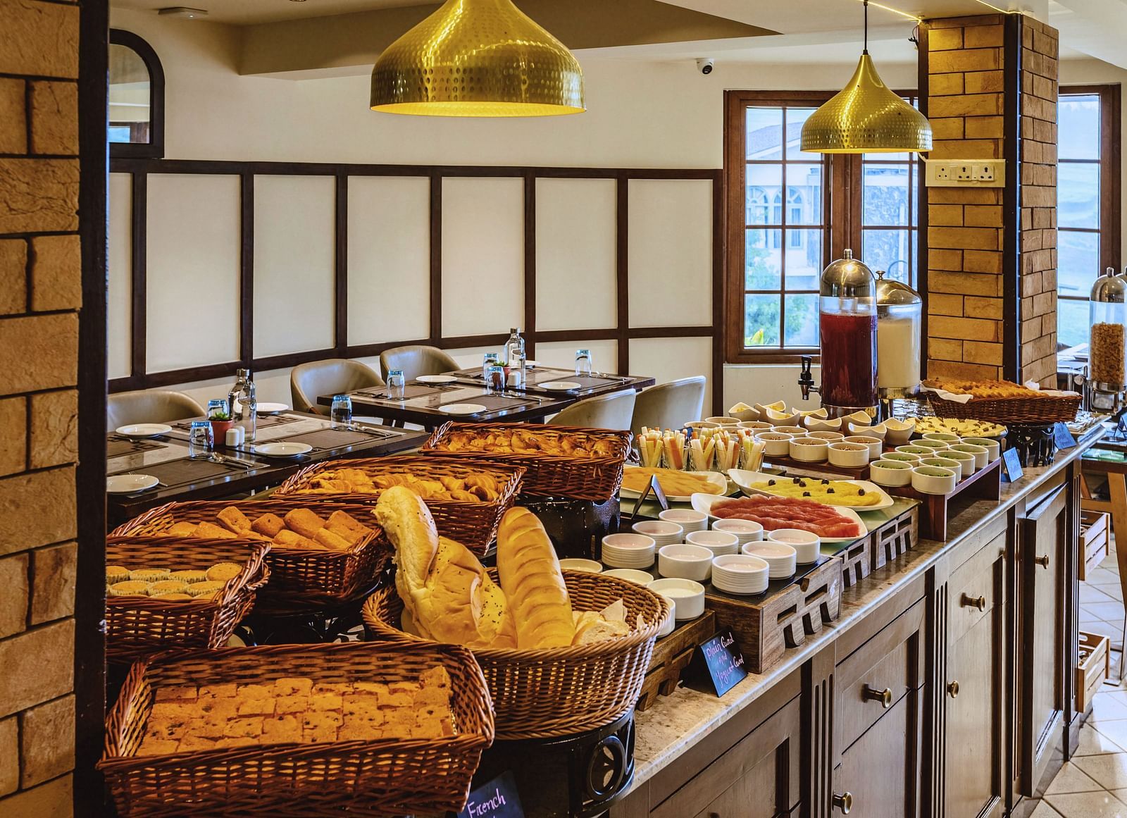 Buffet counter at Mango Hill Shola, Ooty showcasing a wide variety of fresh breads and breakfast items, set under warm pendant lighting.