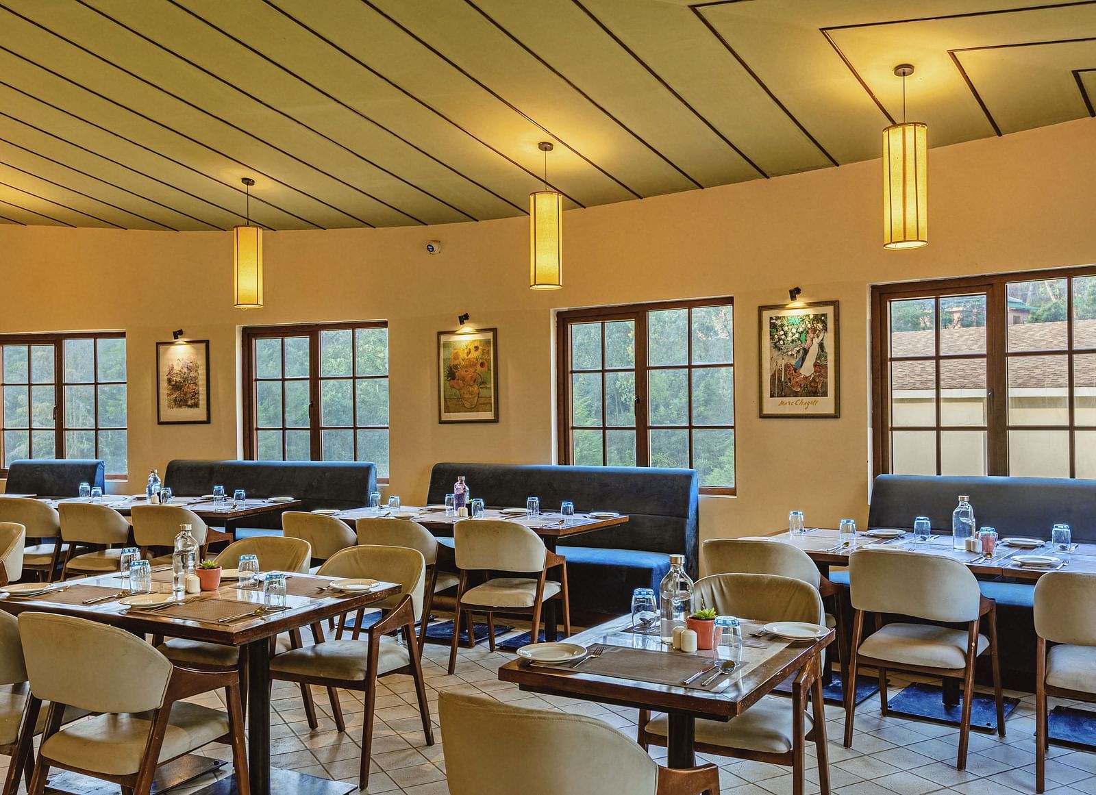 Cosy and well-lit dining space at Mango Hill Shola, Ooty with wooden ceiling accents and window-side tables arranged for a comfortable meal experience.