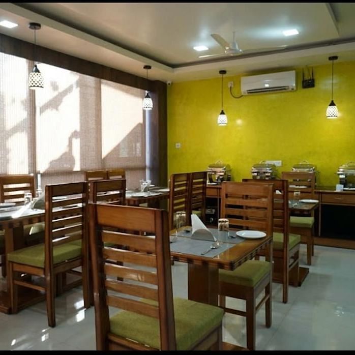 A brightly lit dining space with wooden tables and chairs, perfect for relaxed meals at Pemaling Lords Eco Inn Guwahati.