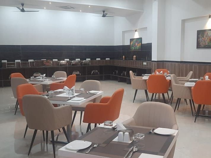 A dining area is set with round tables and orange chairs, with a long table against the wall - Kankidham Lords Inn