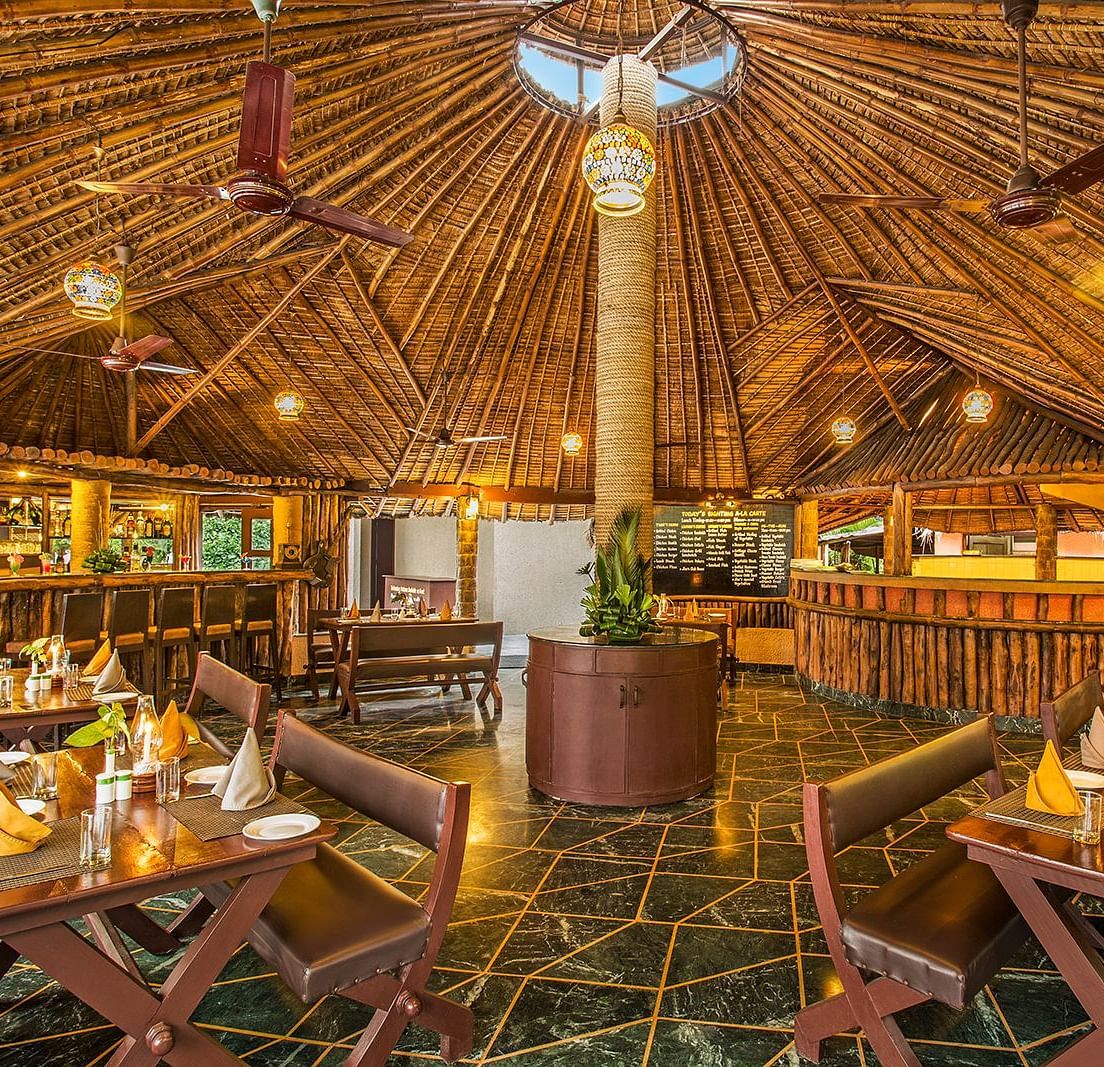 An image of a bar with wooden interiors, wooden chairs and tables, with plants filled at every corner - The Riverview Retreat, Corbett