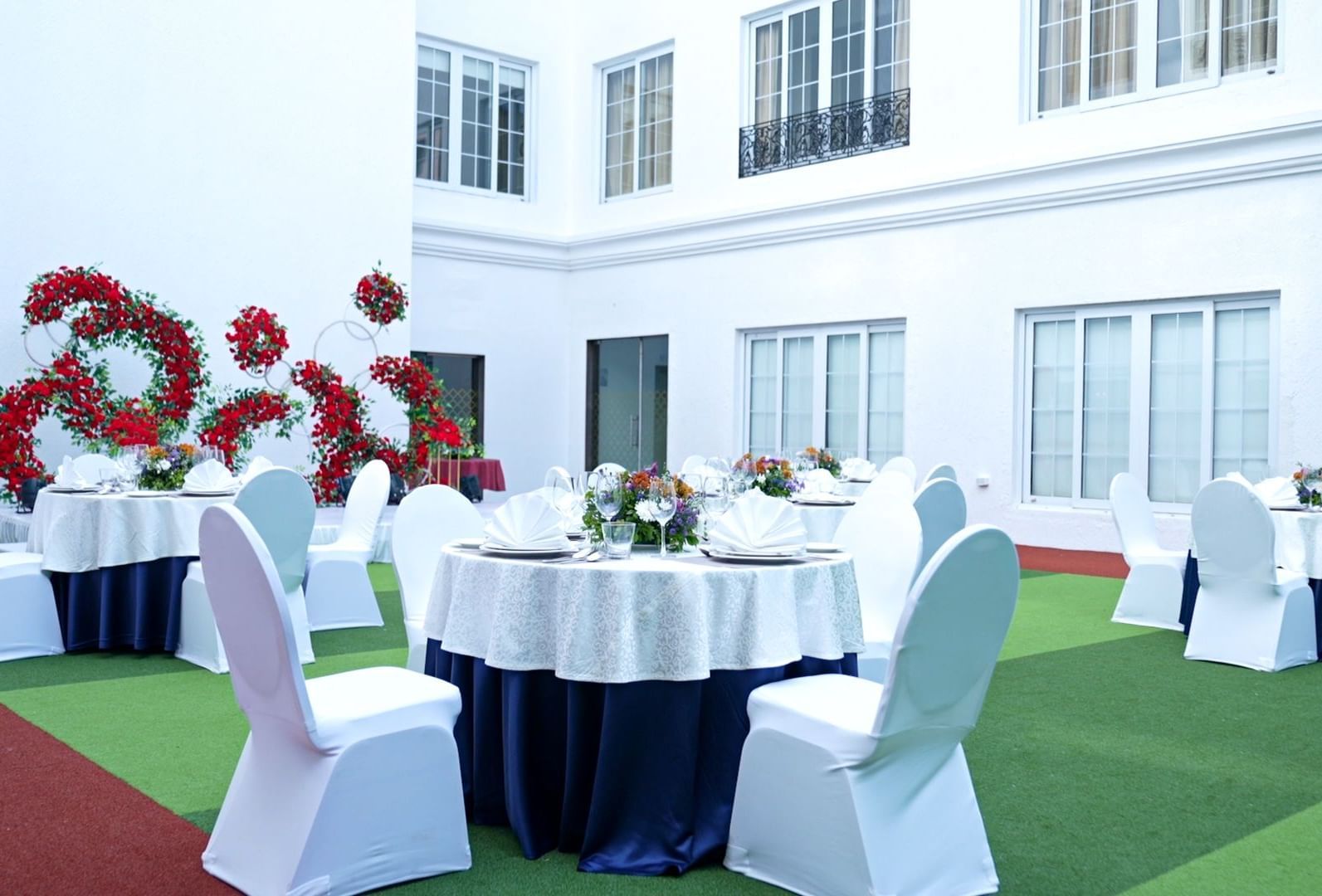 Garden-side banquet arrangement with white tables and chairs, surrounded by a building facade and red floral decor - Accord Chrome Airport Hotel