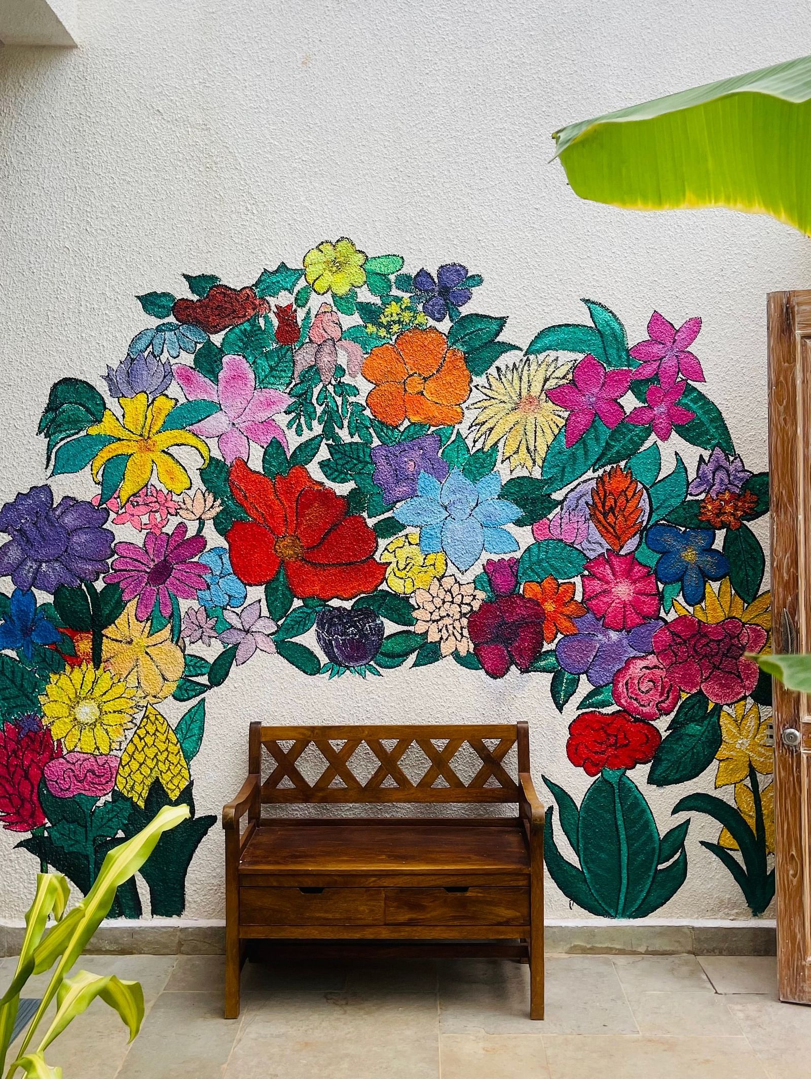 Indoor area at Lindsay Manor with a wooden bench placed in front of a colourful floral wall mural and potted plant nearby.