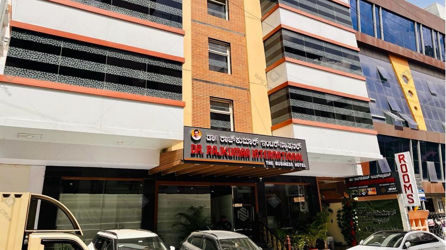 Exterior front view of Hotel Dr Rajkumar International with visible signage, parked vehicles and entrance.