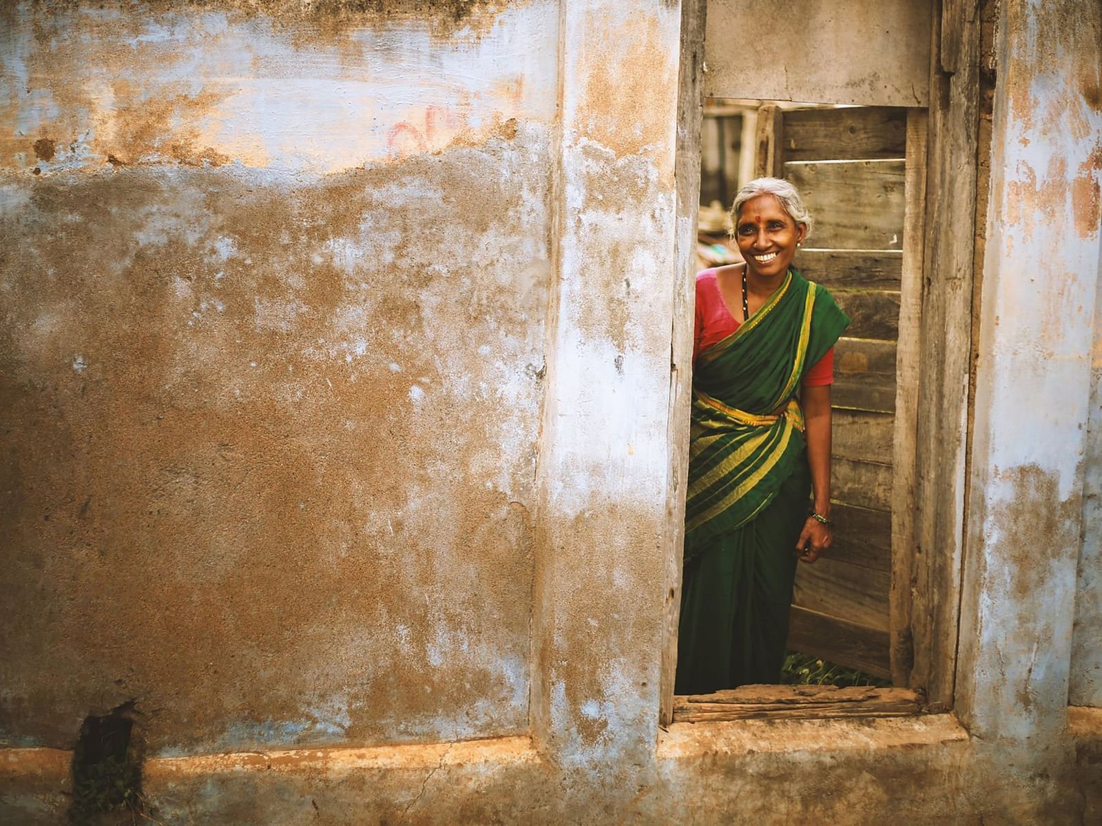 An image of an old lady with a vibrant and welcoming smile standing in a doorway