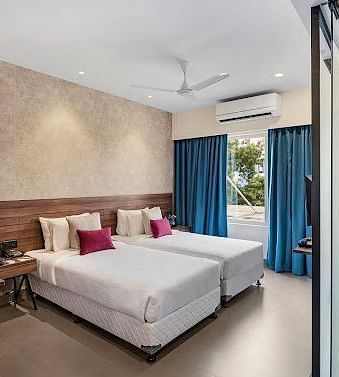 One of our rooms in thoothukudi with twin beds, a table with yellow chairs, and a modern shower area in front - Regency Tuticorin by GRT Hotels