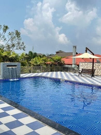 A clear blue swimming pool at Woodstock Resorts, Coorg with a view of the resort's landscaping.