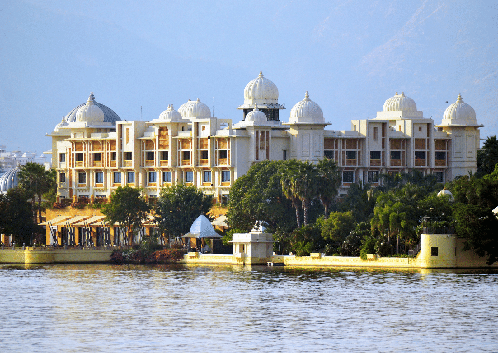 An overview of City Palace in front of Lake Pichola with green trees in front of the building.