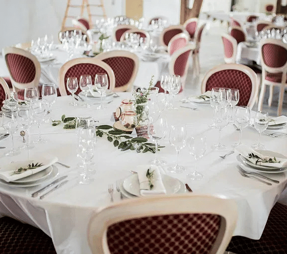 A banquet setup with round tables, white tablecloths, and neatly arranged cutlery and glasses.