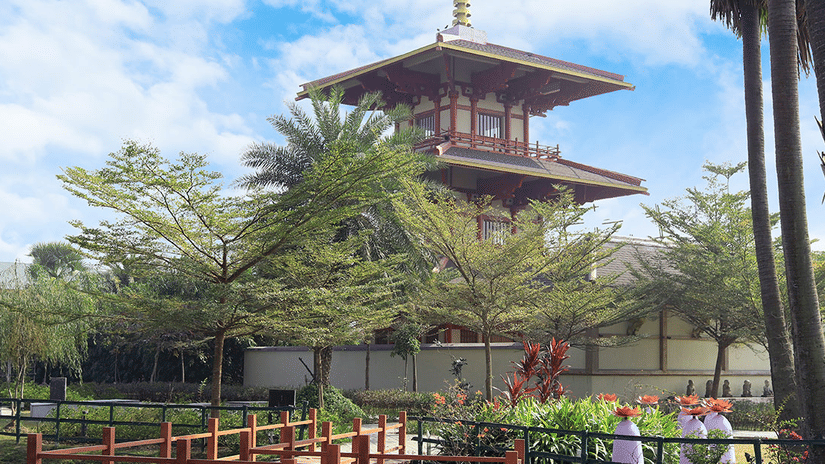 A multi-tiered Japanese pagoda in Eco Park, Kolkata, surrounded by lush green trees and a bright sky.