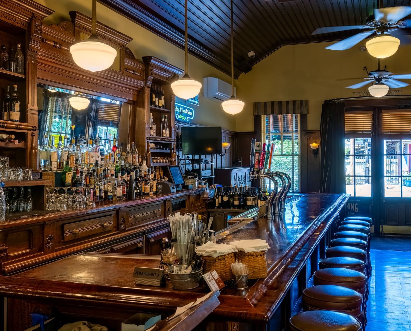 An interior view of Blue Wing Bar at Tallman Hotel with a long wooden counter, stools and various beverages.
