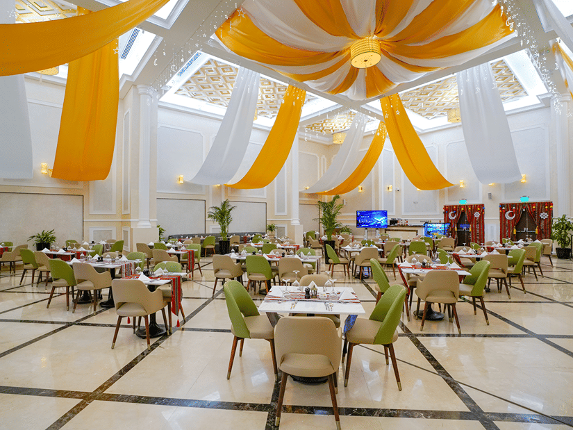 Round table seating inside a banquet hall with white and orange cloth hanging from the ceiling as decoration - La Maison Hotel, Doha