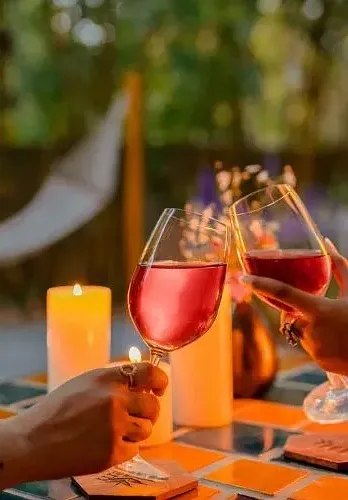 Close-up of two people toasting glasses of rosé wine at an outdoor table with a candle at Karma Chalets.