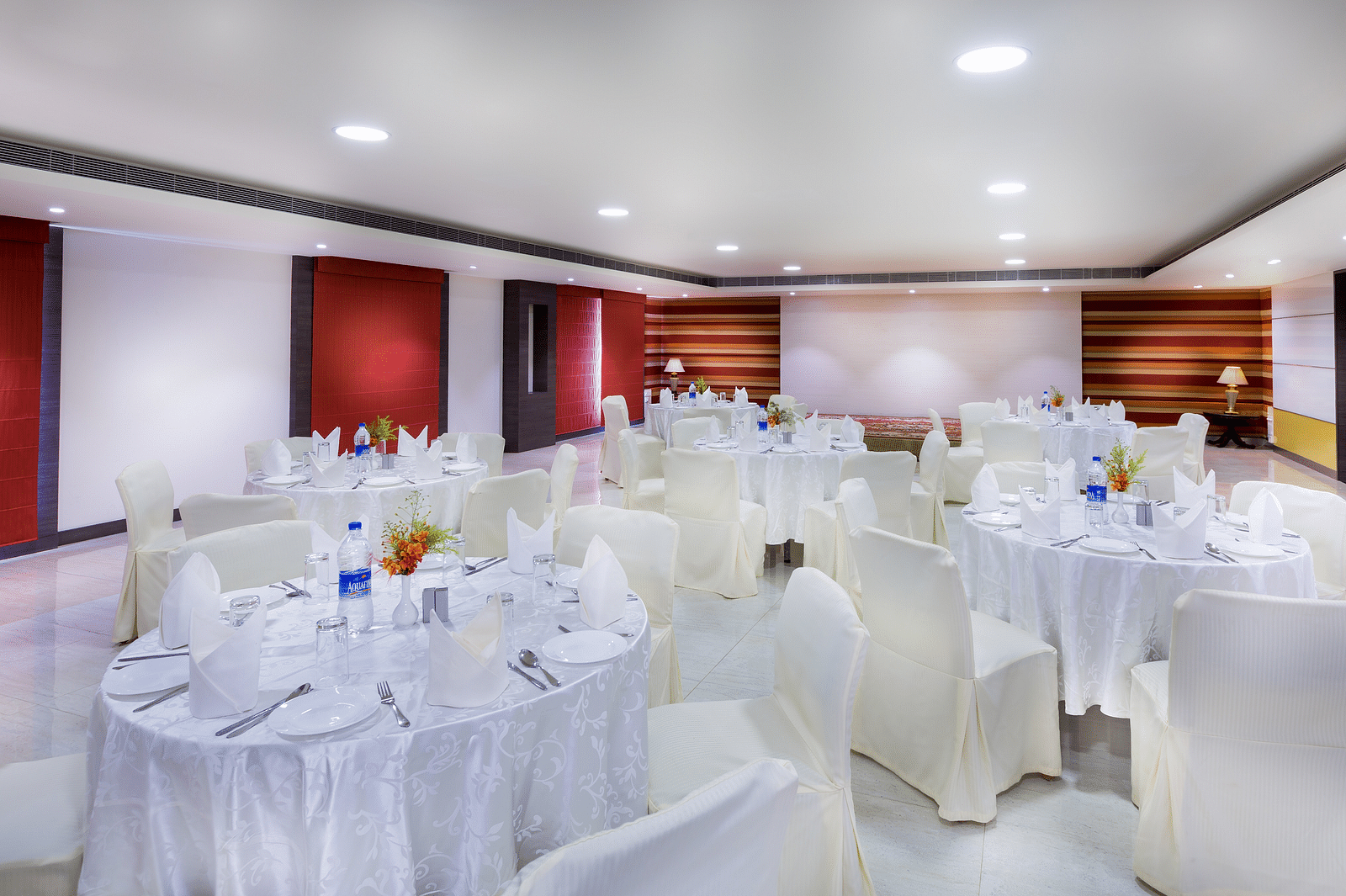 Interiors of a event hall with white chairs and tables at Regency Tiruttani by GRT Hotels.