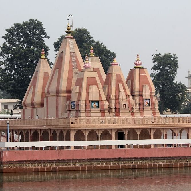 A Hindu temple with multiple domes and a large pond in front, surrounded by trees.