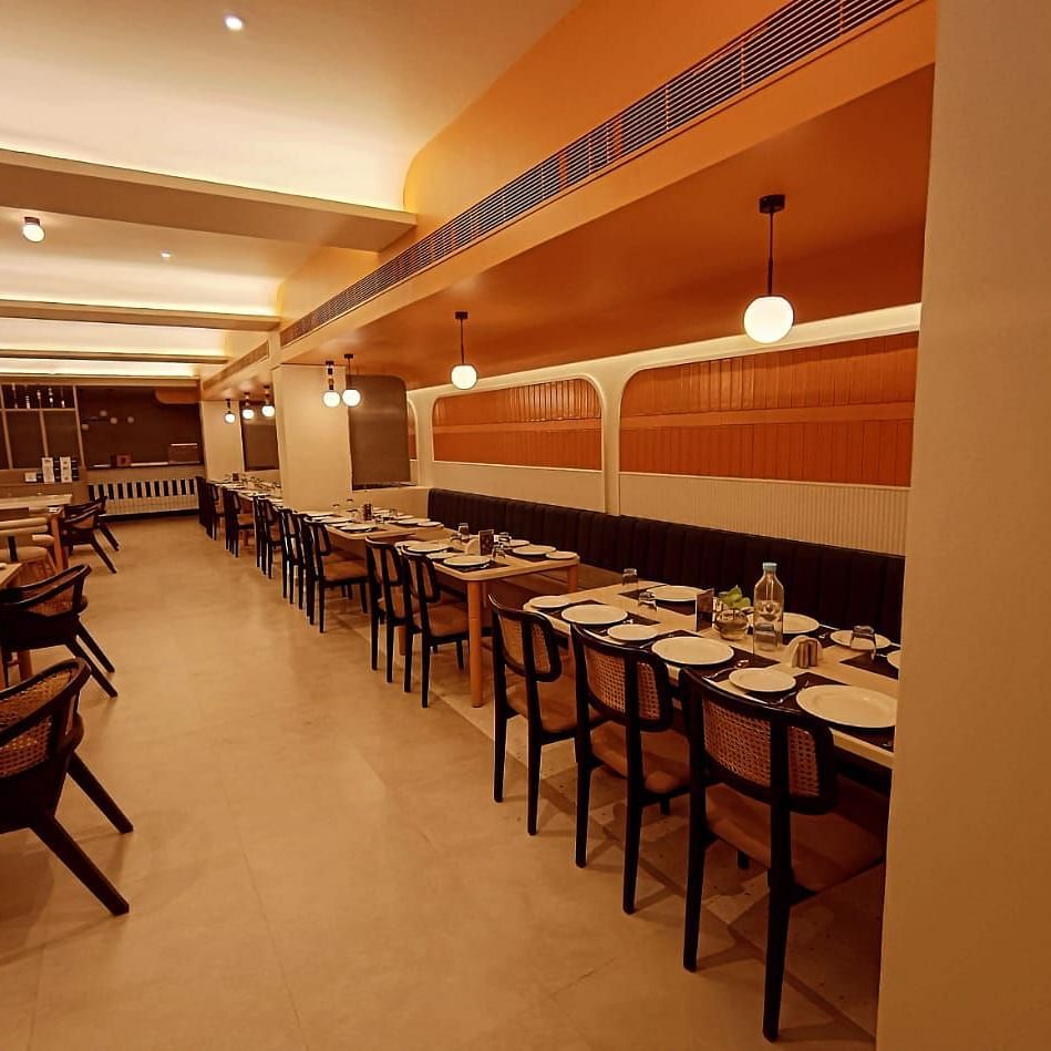 The orange accented dining set-up at Hotel Manorath where dining tables are placed parallel to each other with warm overhead lighting in Lords Eco Inn, Belagavi.