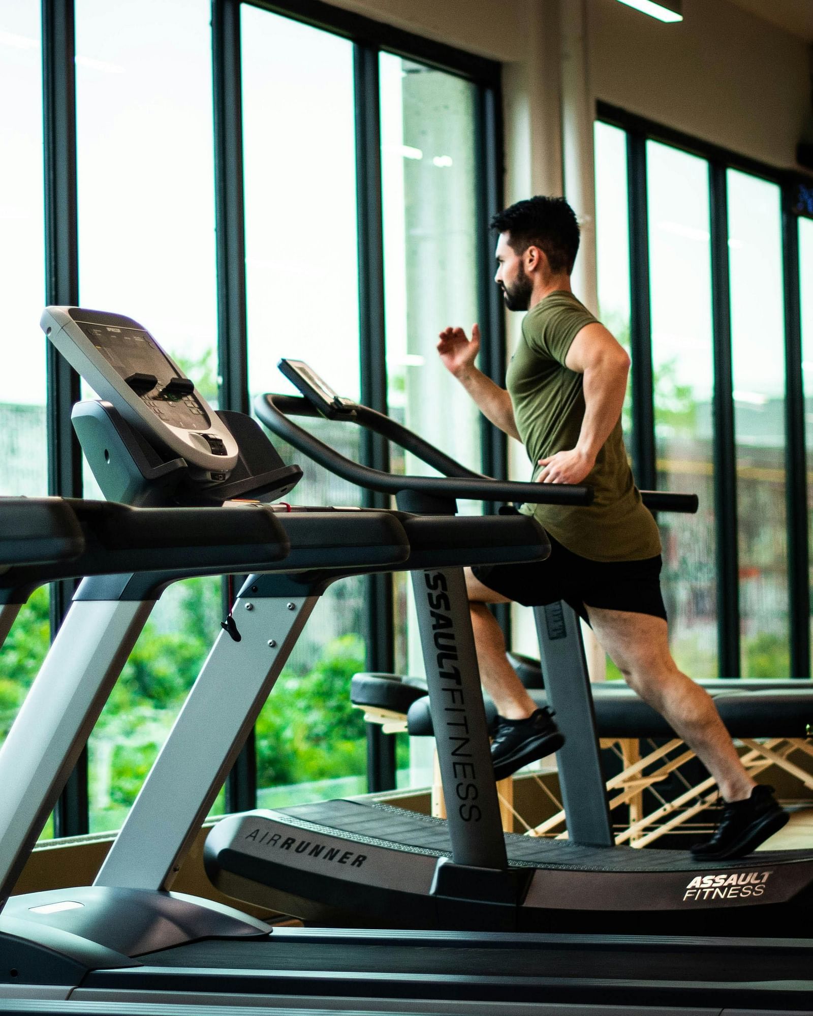 A person exercises on a treadmill in a bright fitness center with large windows at Lords Plaza Surat.