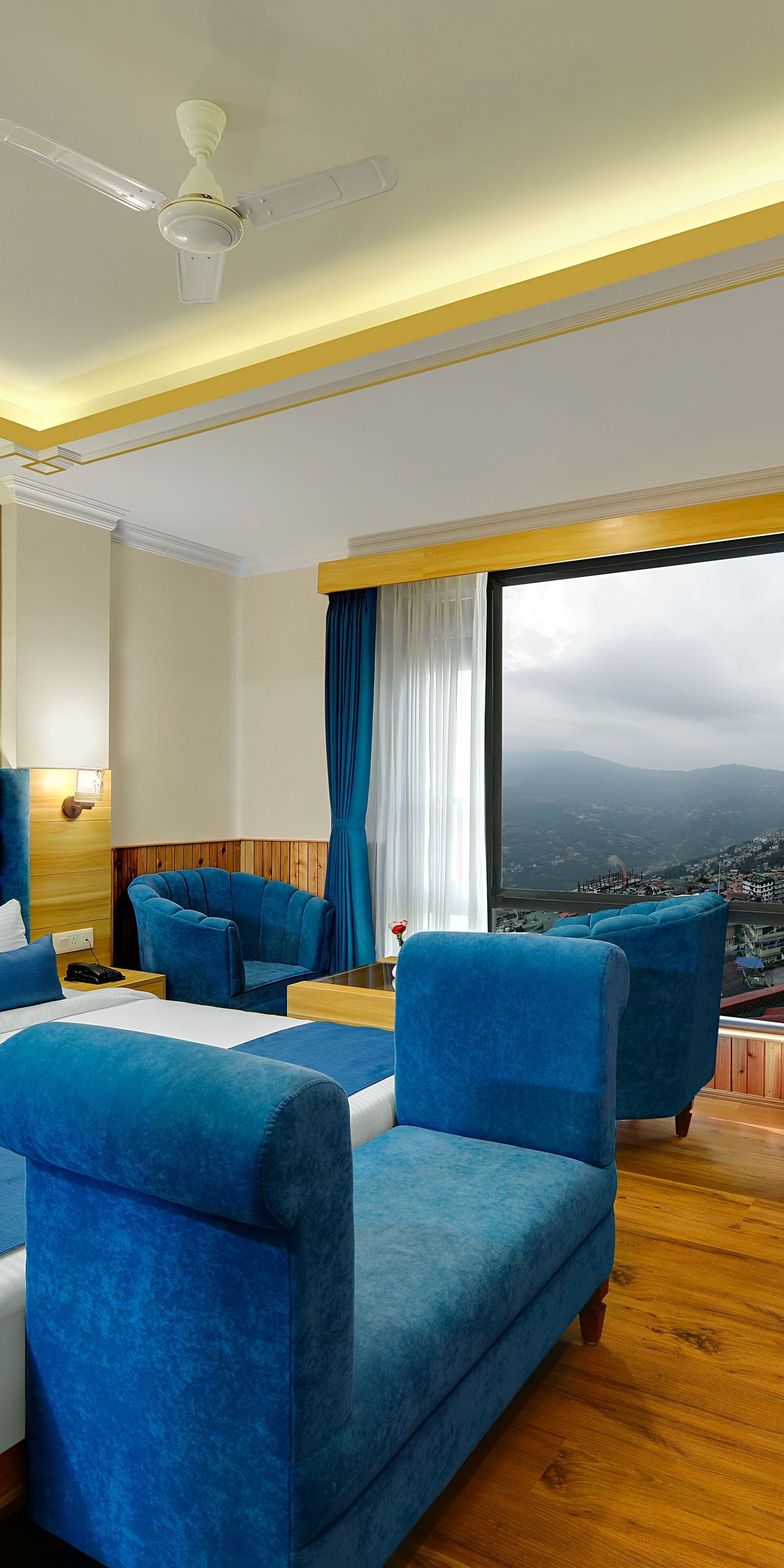 An image of the family suite at Yashshree Sikkim Blossom, Gangtok with a bed, a couch, a sofa set, a table, flat screen TV and an expansive window