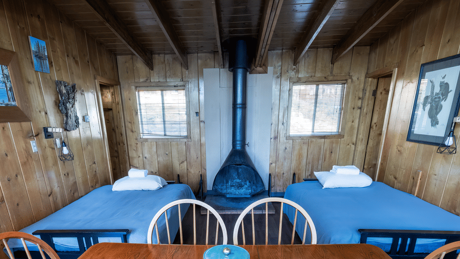 Cabin  room with table , dark blue sheets on beds and rustic wood interiors at Kit Carson Lodge