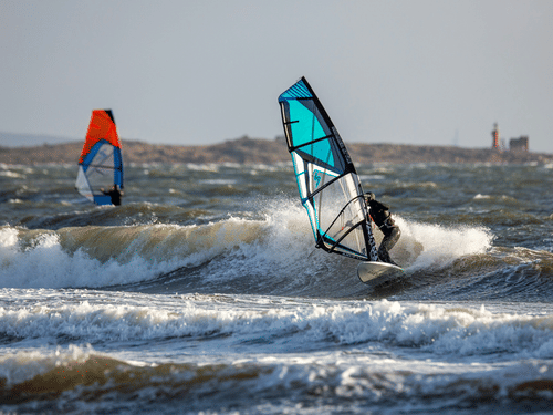 Two people windsurfing across choppy waters, navigating the waves during an exciting water sports adventure.