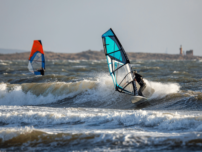 Two people windsurfing across choppy waters, navigating the waves during an exciting water sports adventure.