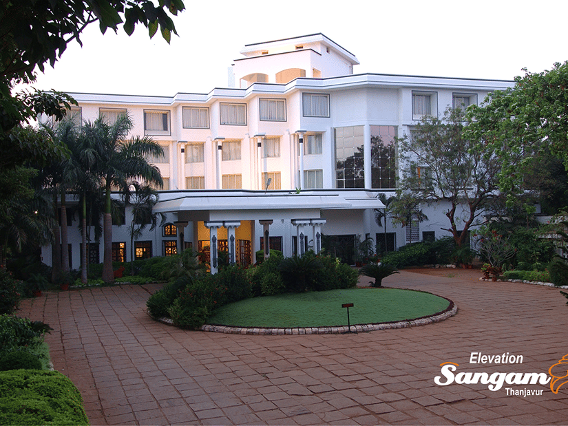 Facade view of Sangam Hotel, Thanjavur, with a pathway, a manicured garden and trees in view - Thanjavur Hotel Contact