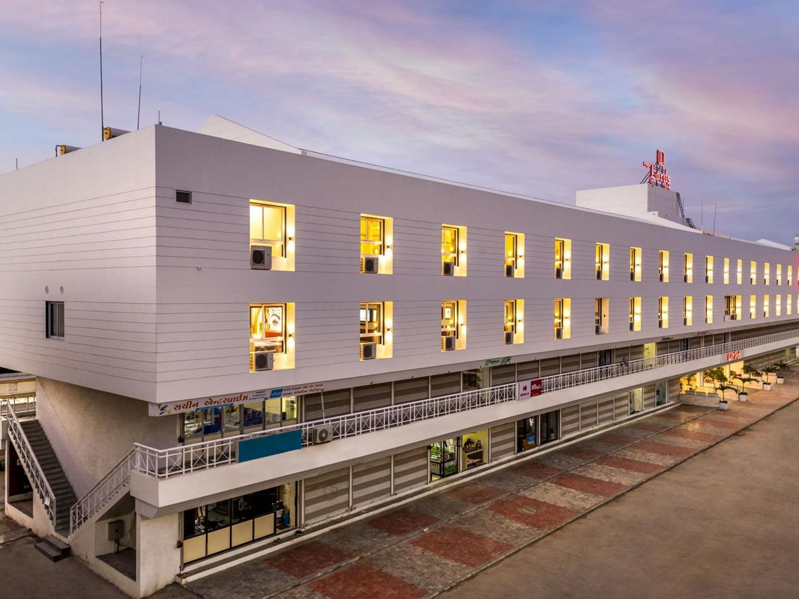 An exterior view at Angel Lords Eco Inn Amreli with many illuminated windows at dusk.