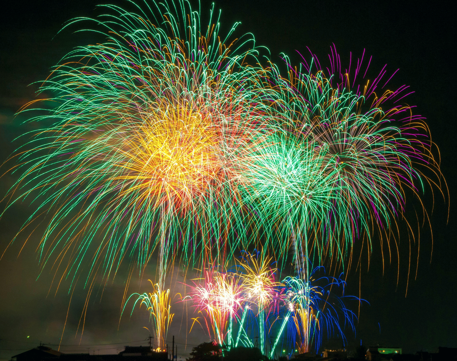 A stunning display of green, yellow, and red fireworks exploding over a dark cityscape at night.
