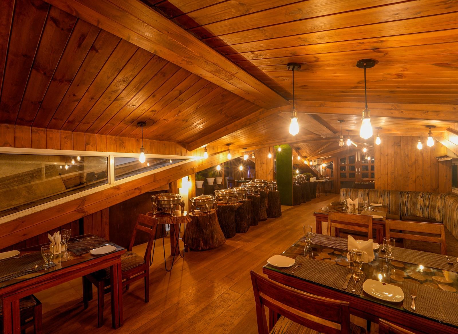 The wooden interiors of the restaurant at DLS Whispering Winds with chairs and tables which it lit with bright lighting