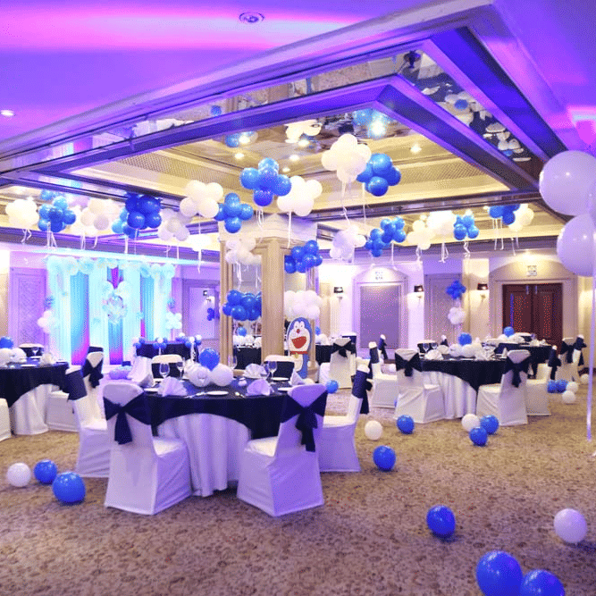 Banquet hall at The Bristol Hotel, Gurgaon decorated for a kids party with round tables in white and navy linen, and balloons floating to a mirrored ceiling.
