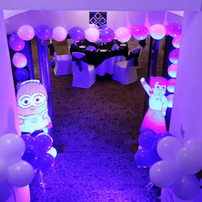 Decorated entrance passage at The Bristol Hotel, Gurgaon with balloon garlands and 2 cartoon cutouts, leading to a table with white chairs.