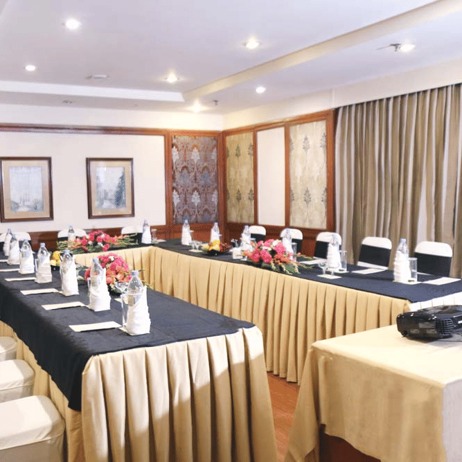 Meeting room at The Bristol Hotel, Gurgaon with a U-shape table in navy and gold linen, a projector on a side table, wall art, and patterned wall panels.