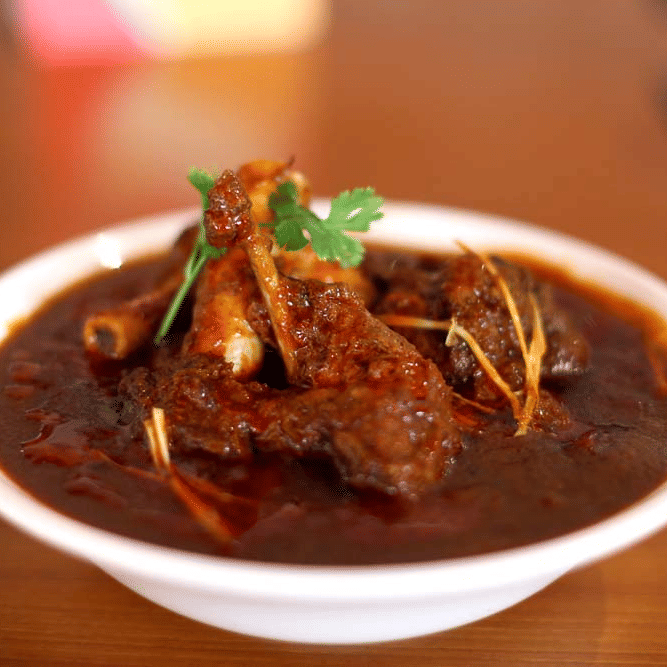 A meat dish in a deep coloured gravy garnished with coriander placed in a bowl on a table at The Bristol Hotel, best choice for a corporate outing in Gurgaon.