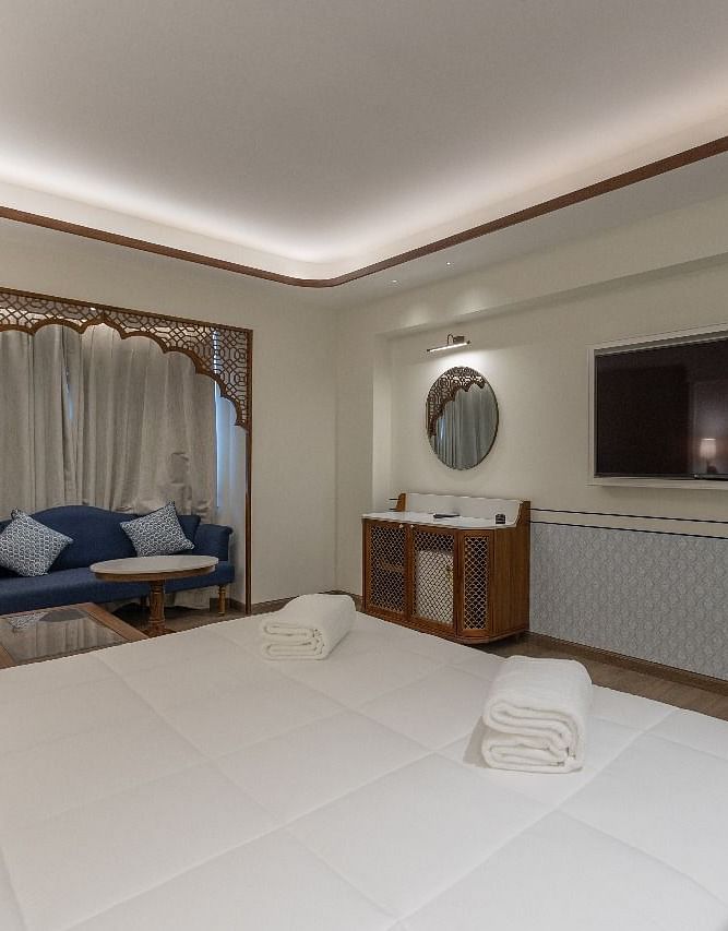 A wide angle shot of the Triveni Room with a luxurious double bed facing a wall mounted television at Bhagirathi by RDB Atishay.