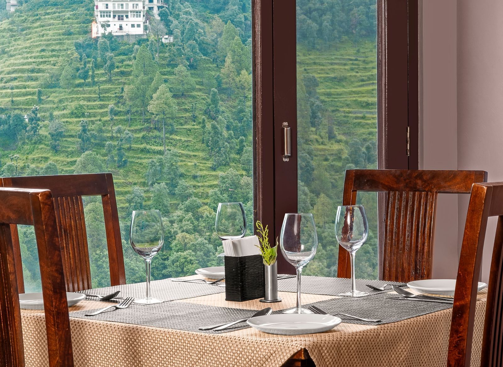 Indoor dining area with a view of terraced hills through large glass windows at BluSalzz Collection - Suvaasa Resort, Ramgarh.