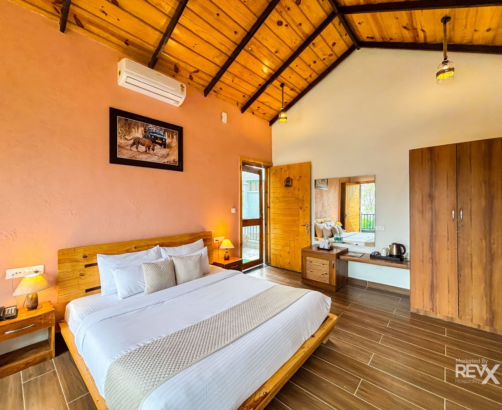 A cosy bedroom with a sloped wooden ceiling, a large bed, and warm-toned walls at Corbett Nirvana Resort..