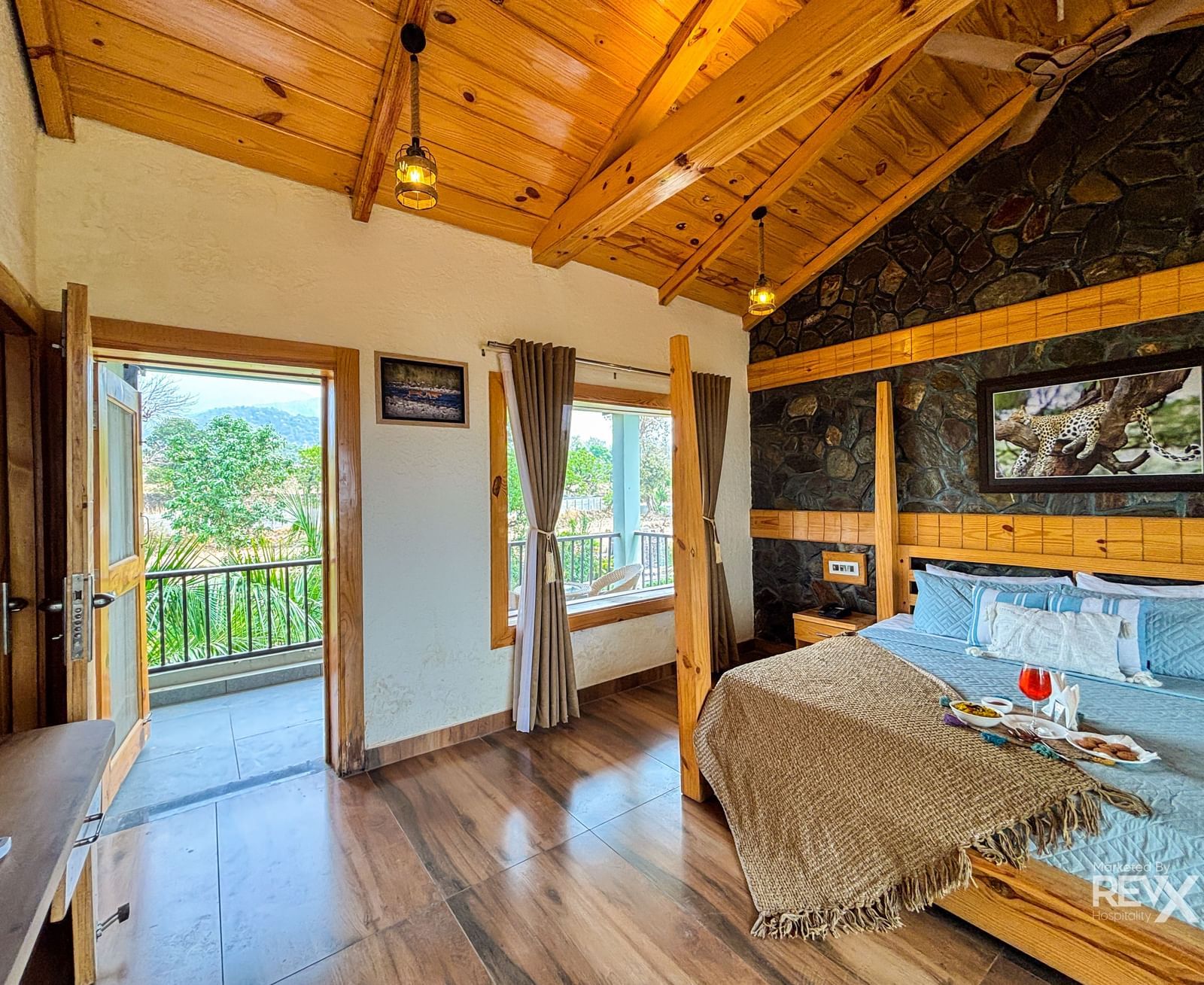 Spacious resort room with wooden ceiling, large windows, and balcony at Corbett Nirvana Resort.