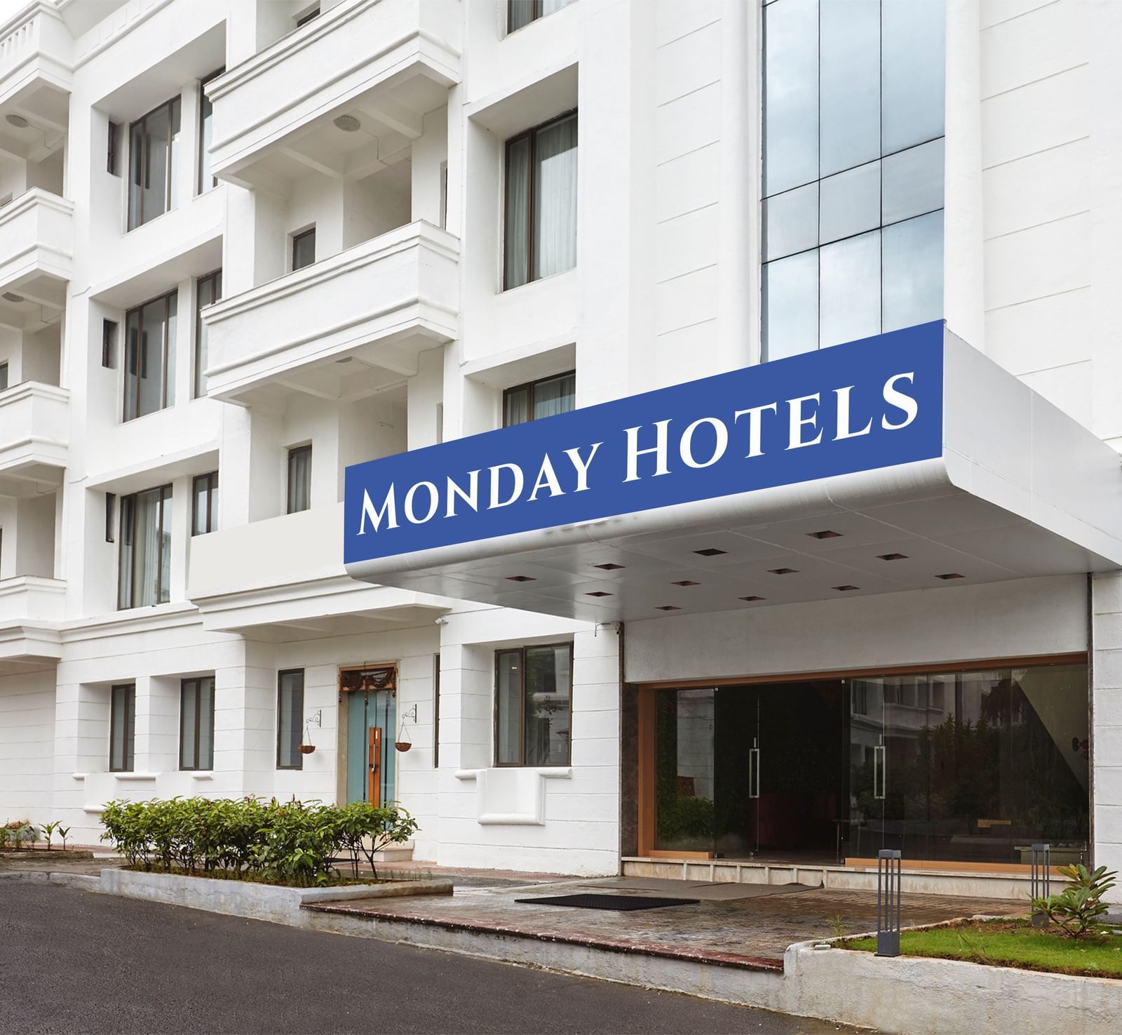The exterior of a hotel building featuring a huge board on the top of the entrance reading 'Monday Hotels' along with a drive way in front of the building.