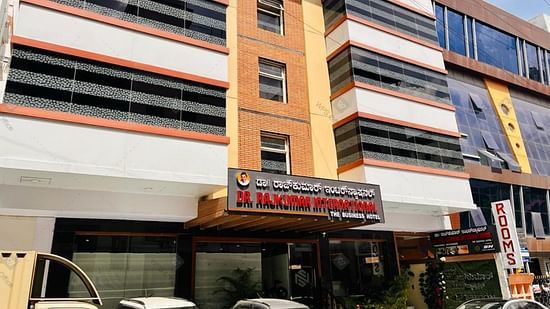 Exterior front view of Hotel Dr Rajkumar International with visible signage, parked vehicles and entrance.